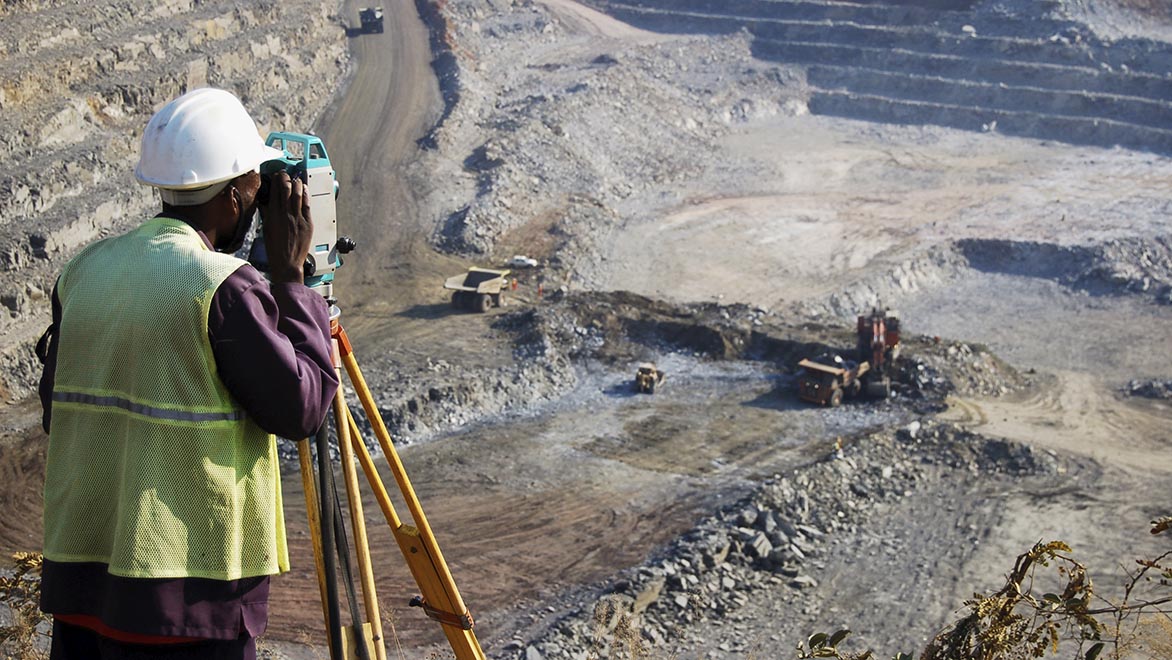 A locally employed surveyor at an open-pit copper mine in Zambia. He peers through his survey instrument to record the daily changes in the open-pit, and help guide mining activities to the engineer's plans.